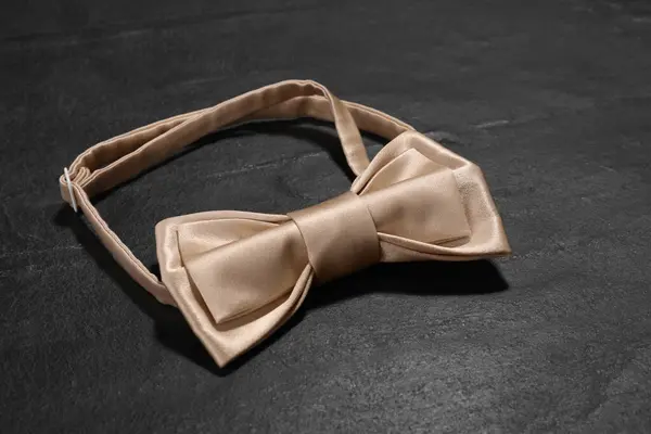 Stylish beige bow tie on black table, closeup