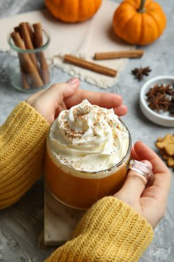 Elinde balkabağı aromalı latte tutan bir kadın açık gri masada kremalı, yakın plan.