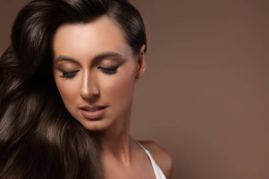 Kahverengi arka planda parlak dalgalı saçları olan muhteşem bir kadın. Mesaj için yer var. Profesyonel kuaförlük