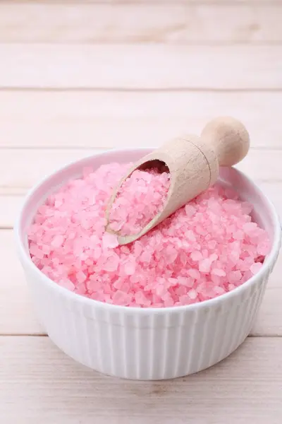 Bowl and scoop with pink sea salt on white wooden table, closeup