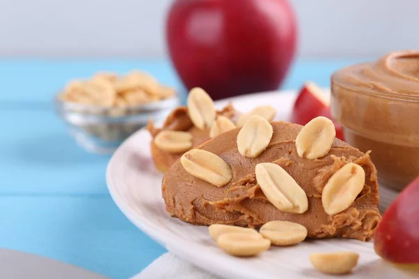 Slice of fresh apple with peanut butter and nuts on light blue wooden table, closeup