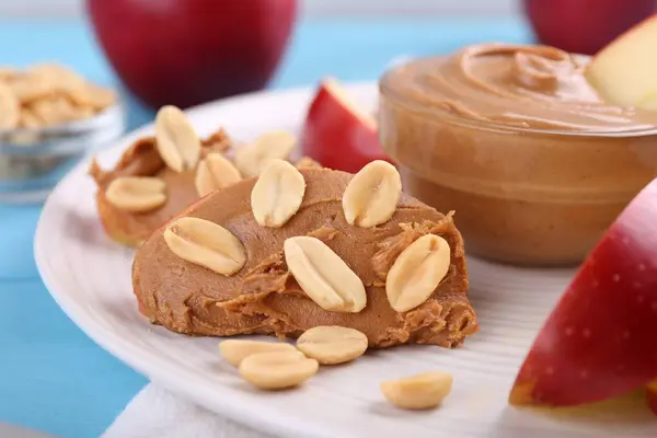 Slices of fresh apple with peanut butter and nuts on light blue table, closeup
