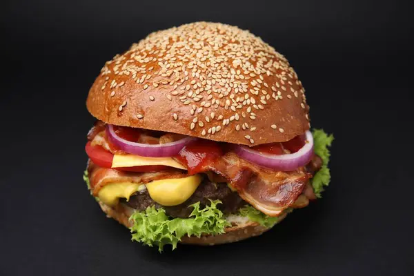 Delicious burger with bacon, patty and vegetables on black background, closeup