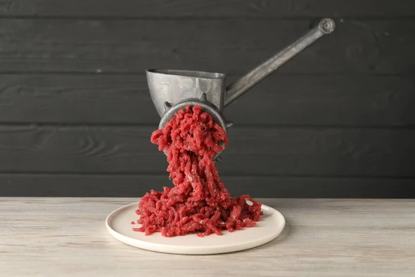Metal meat grinder with beef mince on light wooden table
