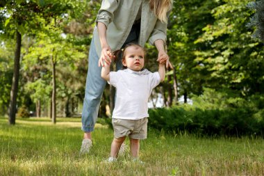 Anne kızına destek olurken parkta yürümeyi öğreniyor, yakın plan.