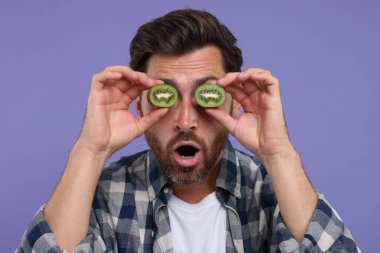 Mor arka planda gözlerinin yanında kivi parçaları tutan duygusal bir adam.