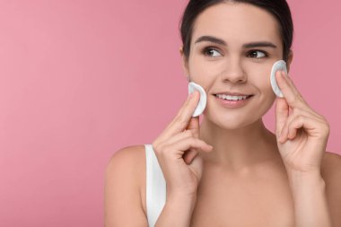 Pembe arka planda pamuk pedlerle yüzünü temizleyen genç bir kadın. Metin için boşluk