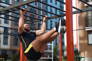 Young man training on monkey bars at outdoor gym clipart