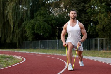 Stadyumda elastik direniş bandıyla egzersiz yapan kaslı adam.