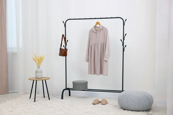 Clothing rack with stylish dress, bag and shoes in room