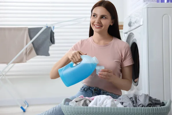Woman pouring fabric softener from bottle into cap near washing machine in bathroom, space for text