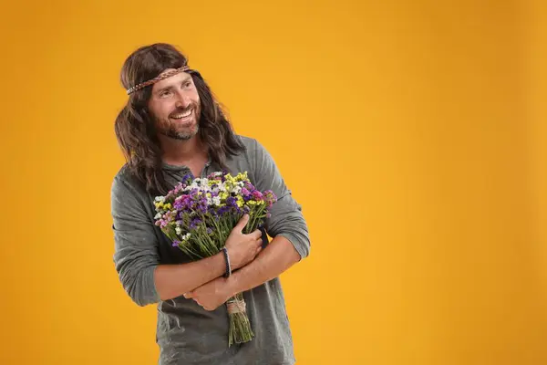 Hippie man with bouquet of colorful flowers on orange background, space for text