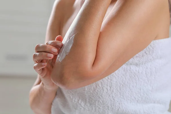 Woman applying body cream onto arm on blurred background, closeup