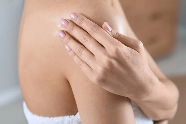 Woman applying body oil onto shoulder indoors, closeup