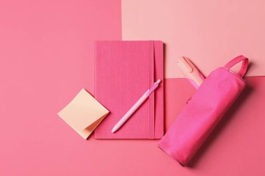 Pembe zemin üzerinde diğer kırtasiye malzemesi ile parlak defter ve çanta, düz yatıyordu