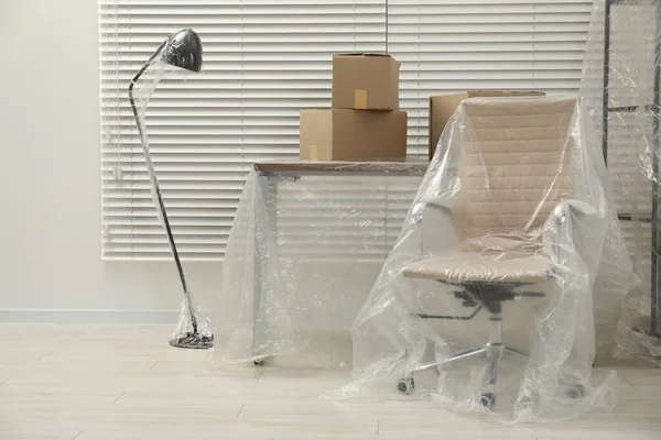 Modern furniture covered with plastic film and boxes at home