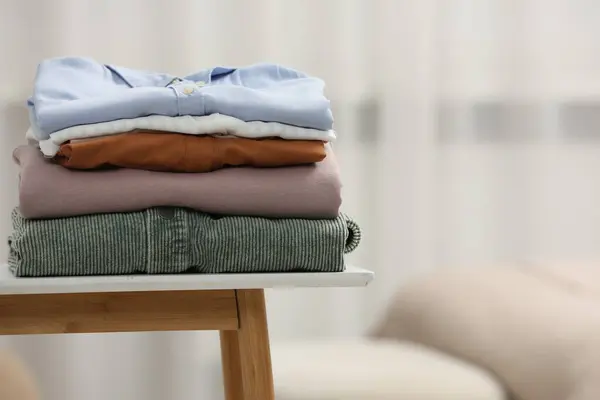 Stack of different folded clothes on bedside table indoors, closeup. Space for text