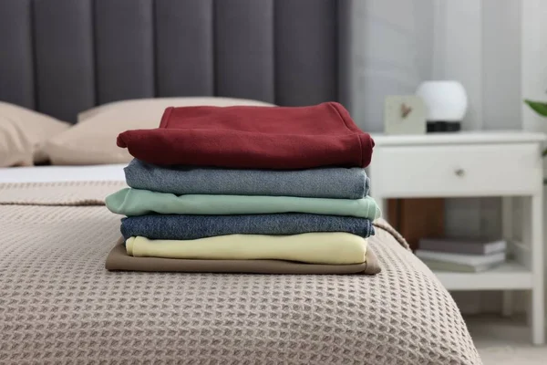 Stack of different folded clothes on bed at home