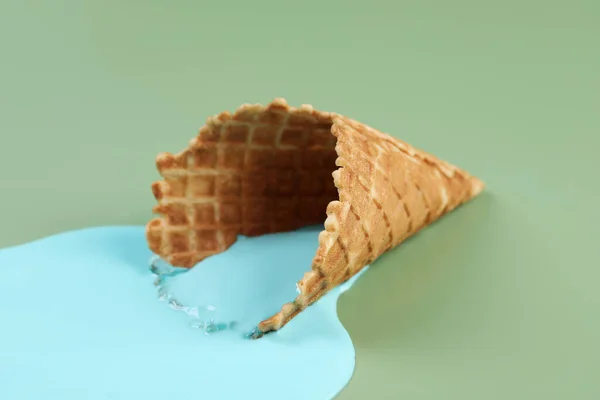 Melted ice cream and wafer cone on green background, closeup