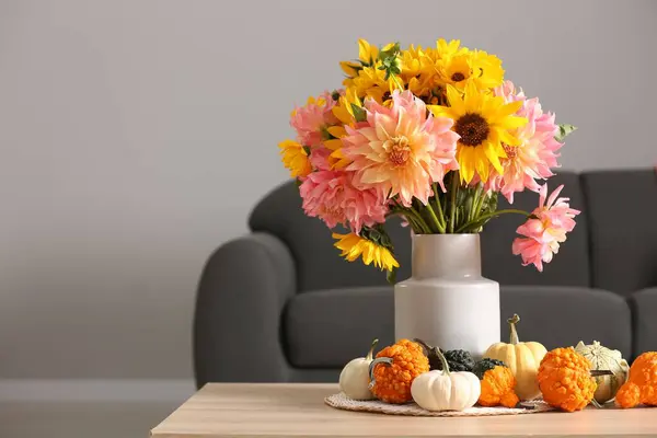 Autumn mood. Beautiful bouquet with bright flowers and small pumpkins on wooden table in room, space for text