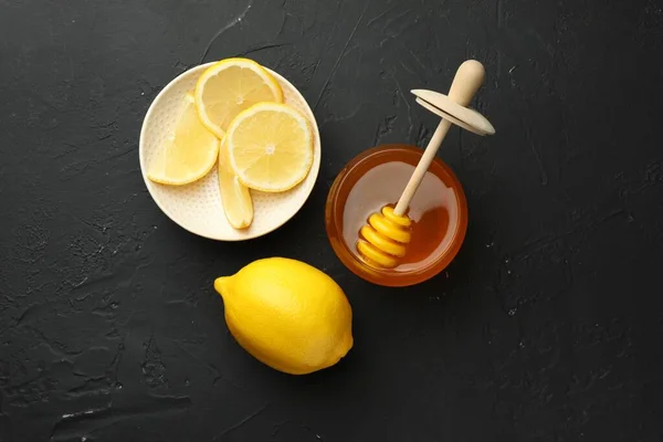 Sweet honey and fresh lemons on black table, flat lay