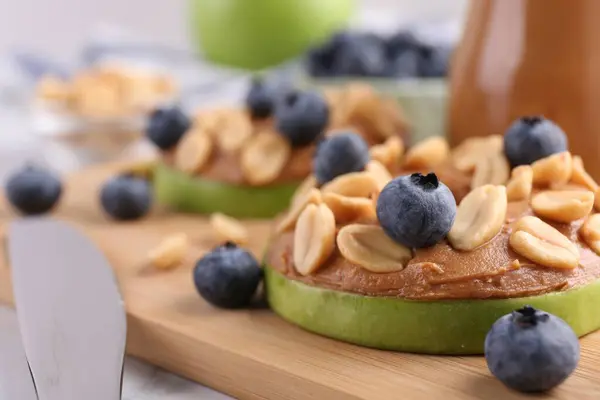 Slice of fresh apple with peanut butter, blueberries and nuts on table, closeup