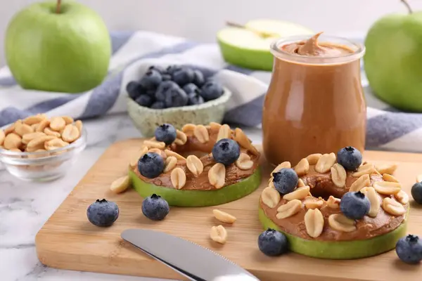 Slices of fresh apple with peanut butter, blueberries and nuts on white marble table, closeup