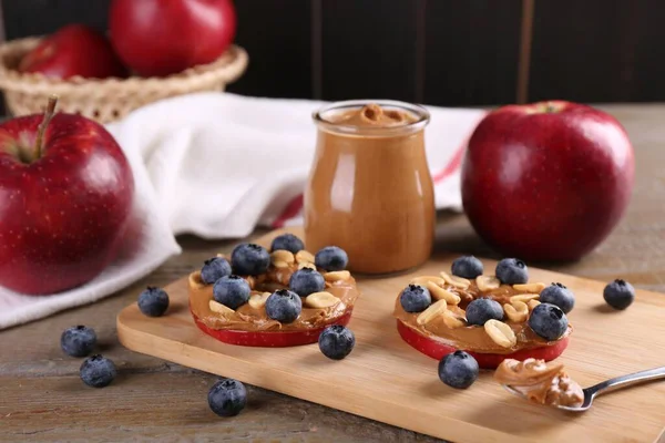 Slices of fresh apple with peanut butter and blueberries on wooden table