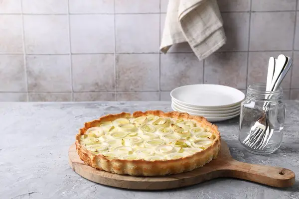 Freshly baked leek pie, forks and plates on grey textured table. Space for text