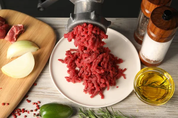 Metal meat grinder with minced beef and spices on light wooden table