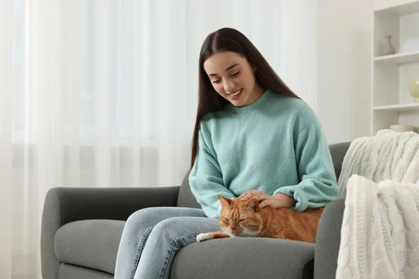 Beautiful woman petting cute cat on sofa at home, space for text