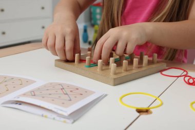 Motor beceri geliştirme. Beyaz masada coğrafya ve lastik bantlarla oynayan kız, yakın plan.