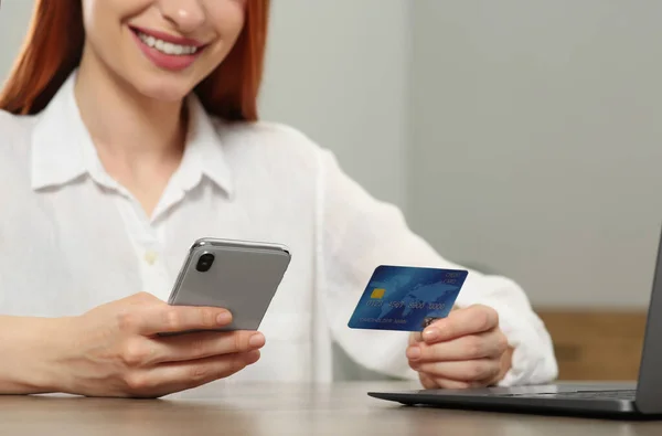 Woman with credit card using smartphone for online shopping at wooden table indoors, closeup