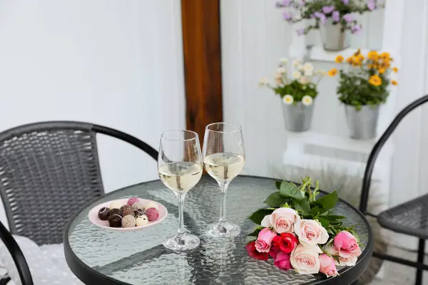 Bouquet of roses, glasses with wine and candies on glass table on outdoor terrace