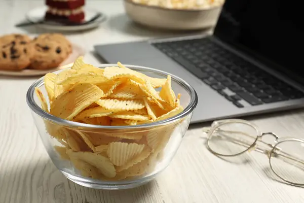 Bad eating habits at workplace. Tasty ridged chips in bowl on white wooden table, closeup