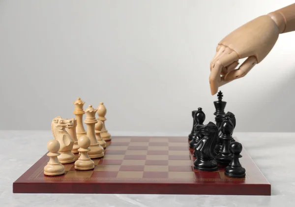 Robot playing chess against light grey background, closeup. Wooden hand representing artificial intelligence