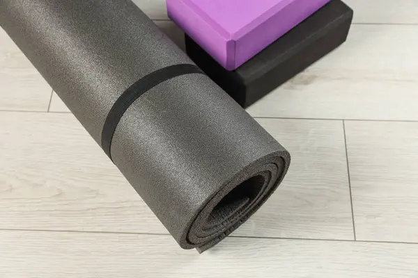 Exercise mat and yoga blocks on light wooden floor, closeup