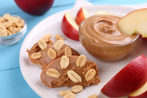 Slices of fresh apple with peanut butter and nuts on light blue wooden table, closeup