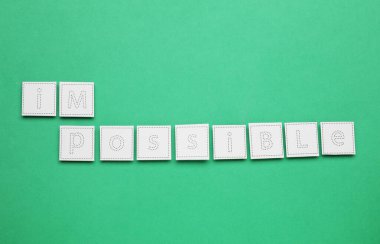 Motivasyon konsepti. Yeşil arkaplan üzerinde I ve M harfleri olan kağıdı kaldırarak sözcüğü imkansızdan olanaksıza çevirmek, üst görünüm