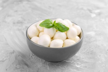 Lezzetli mozarella topları ve fesleğen yaprakları gri masada, yakın plan.