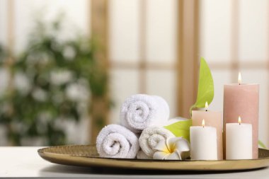 Spa kompozisyonu. Yanan mumlar, tesisat çiçeği, yeşil yapraklar ve havlular beyaz masa içinde, yazı için yer