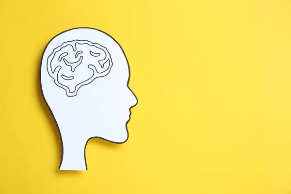 Paper human head cutout with drawing of brain on yellow background, top view. Space for text