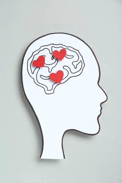 Emotional thinking. Paper human head cutout with drawing of brain and red hearts on grey background, top view