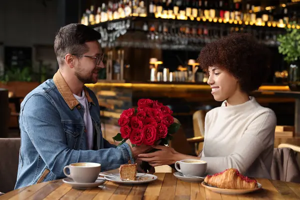 International dating. Handsome man presenting roses to his girlfriend in cafe