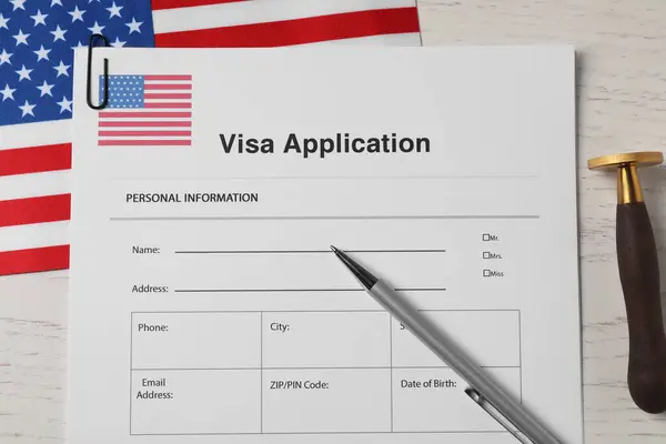 Immigration to USA. Visa application form, flag, stamp and pen on white wooden table, flat lay