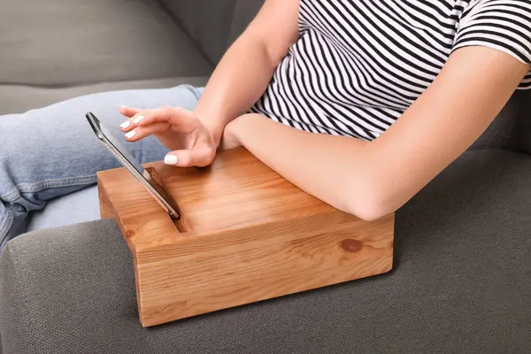 Woman using smartphone on sofa armrest wooden table at home, closeup