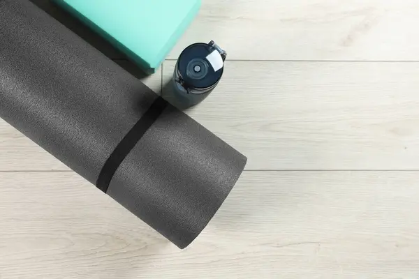 Exercise mat, yoga block and bottle of water on light wooden floor, flat lay. Space for text