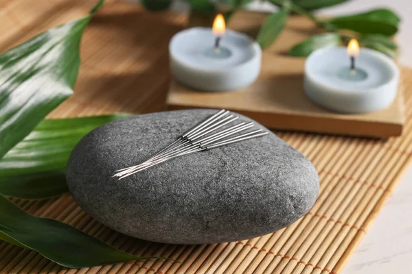 Stone with acupuncture needles and burning candles on table, closeup