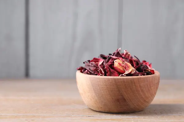 Dry hibiscus tea in bowl on wooden table, space for text