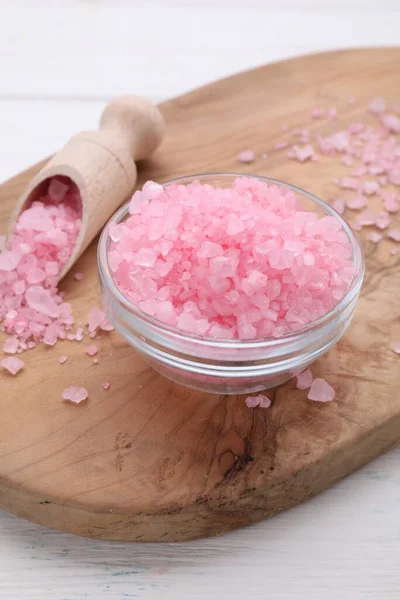 Bowl and scoop with pink sea salt on white wooden table, closeup